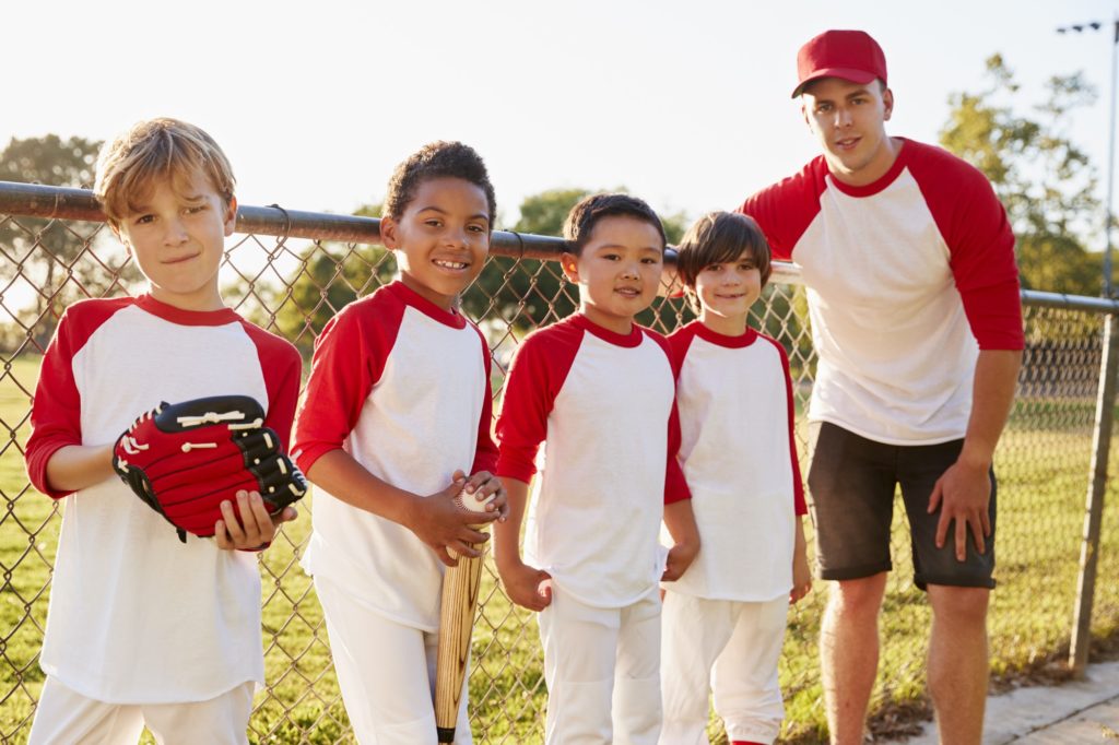 Coach and young boys in a baseball team looking to camera