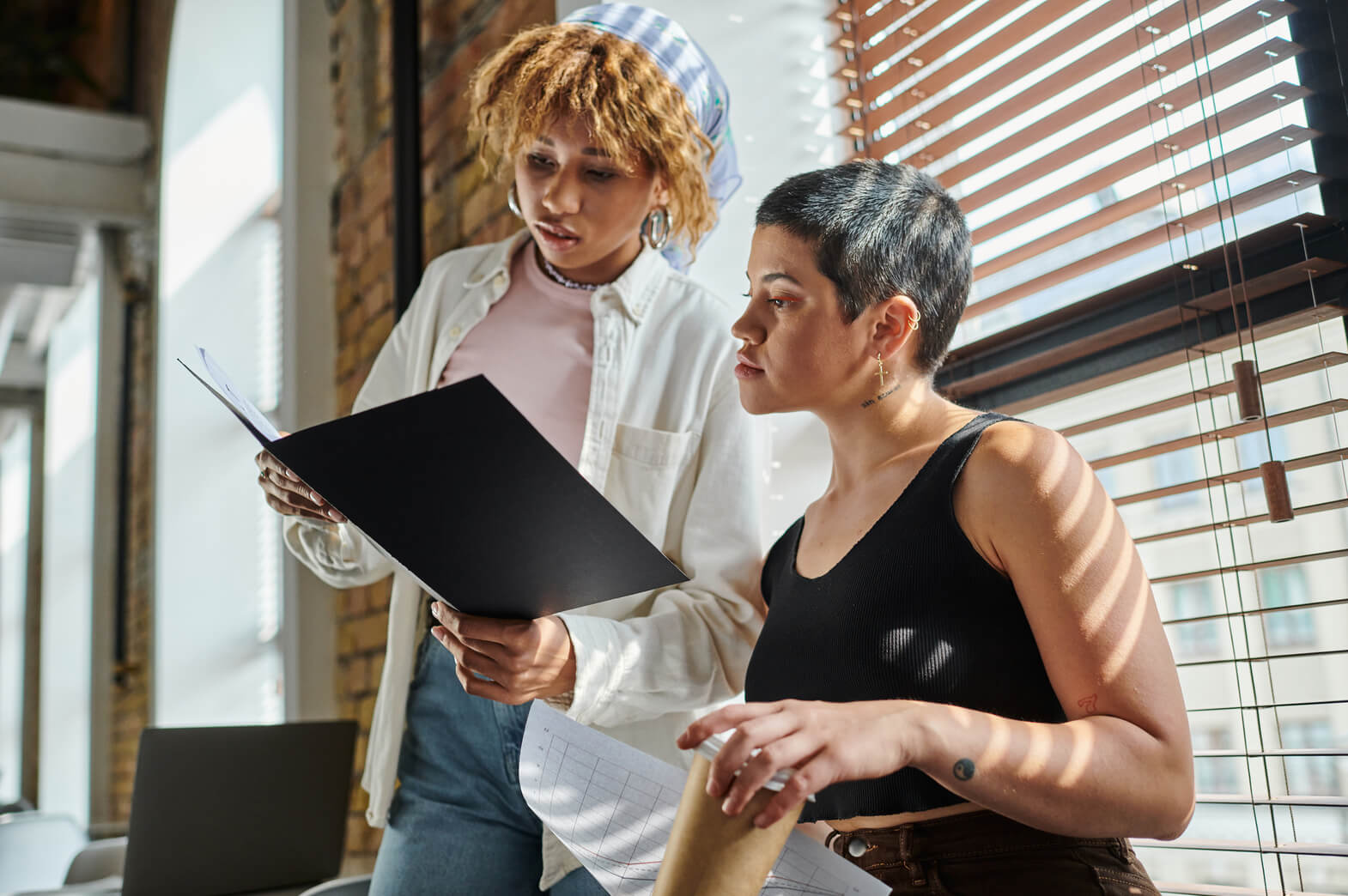 A woman shows her coworker a folder of documents