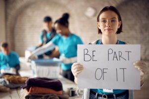Young volunteer holding placard with 'be part of it message' at charitable foundation.